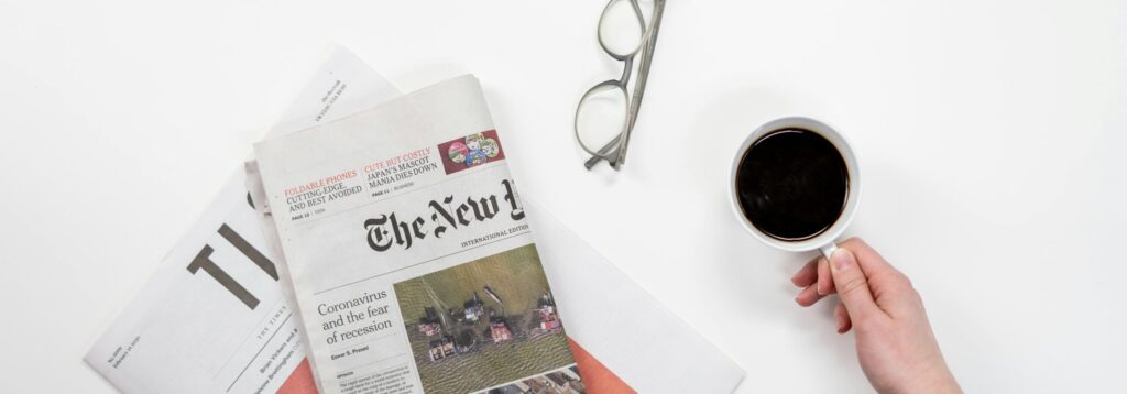 Top view of a coffee cup, newspapers, and eyeglasses on a clean white desk, ideal for a morning routine theme.