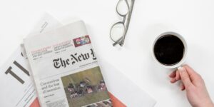 Top view of a coffee cup, newspapers, and eyeglasses on a clean white desk, ideal for a morning routine theme.