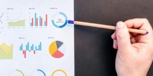 Hand holding pencil reviewing colorful data charts on desk with laptop.